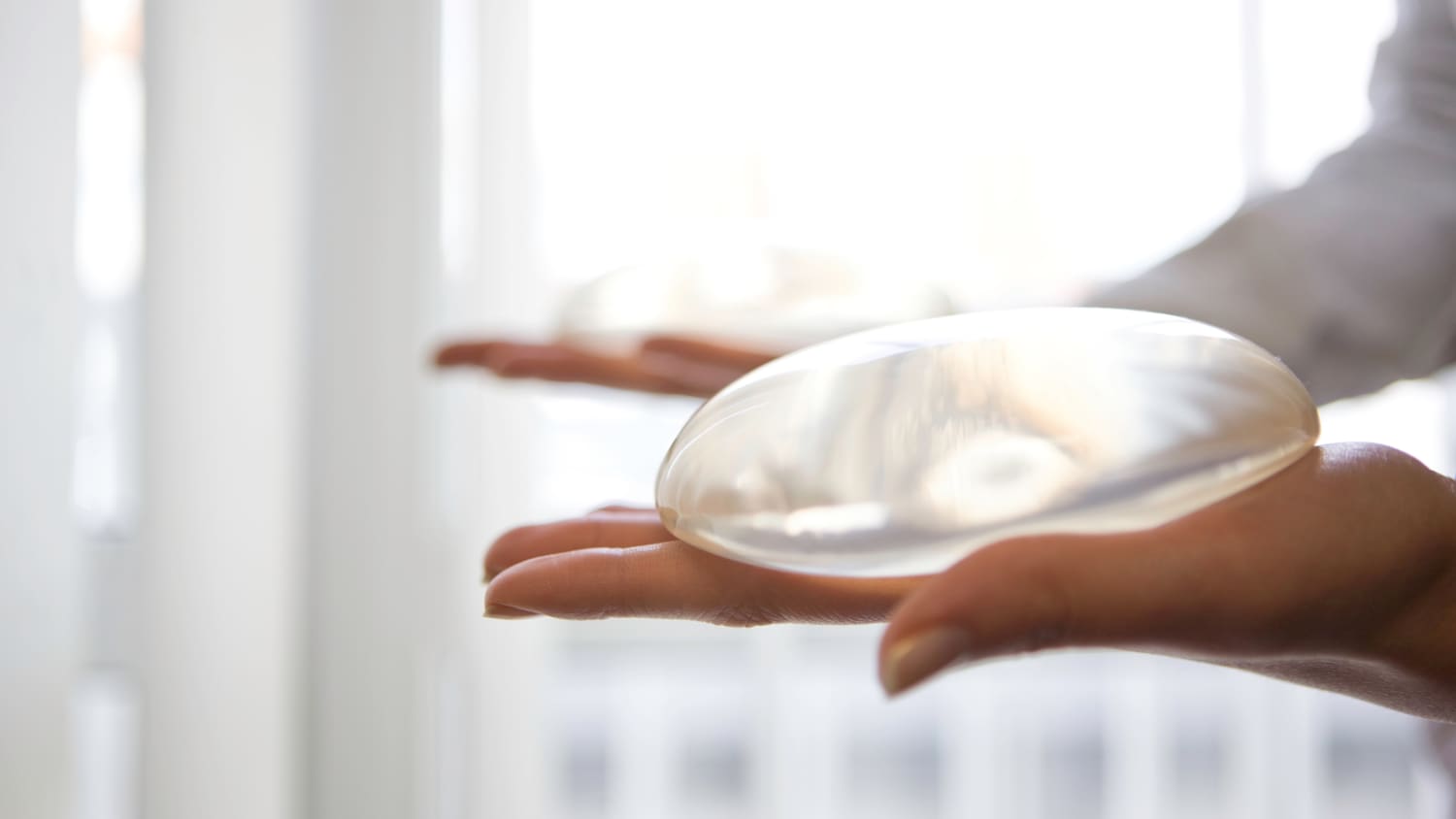 Hands holding a round, silicone breast implant.