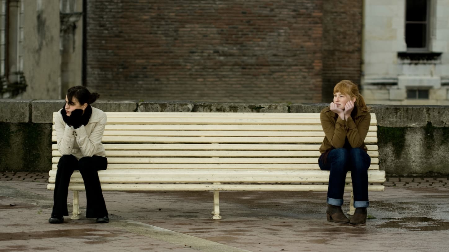 two girls on opposite sides of a bench, practicing social distancing during COVID-19 pandemic