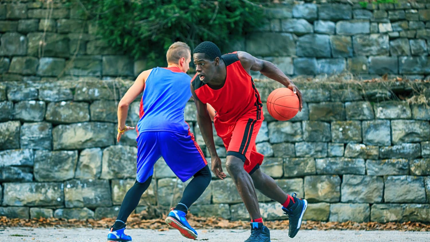 Two young people play basketball in a park.