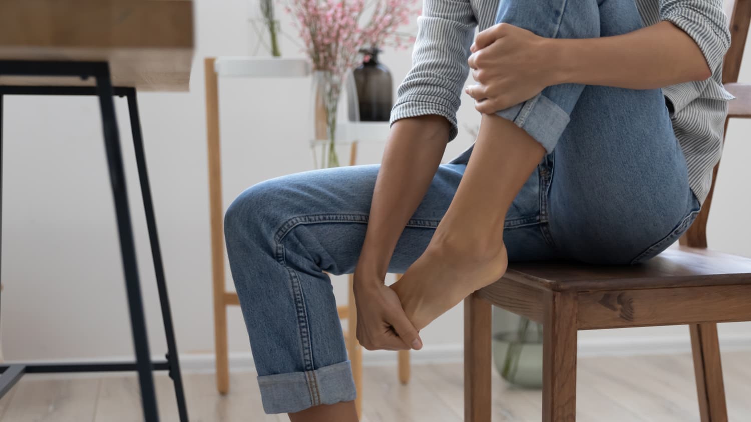 woman sitting in chair with foot pain, possibly from tendonitis or plantar fasciitis