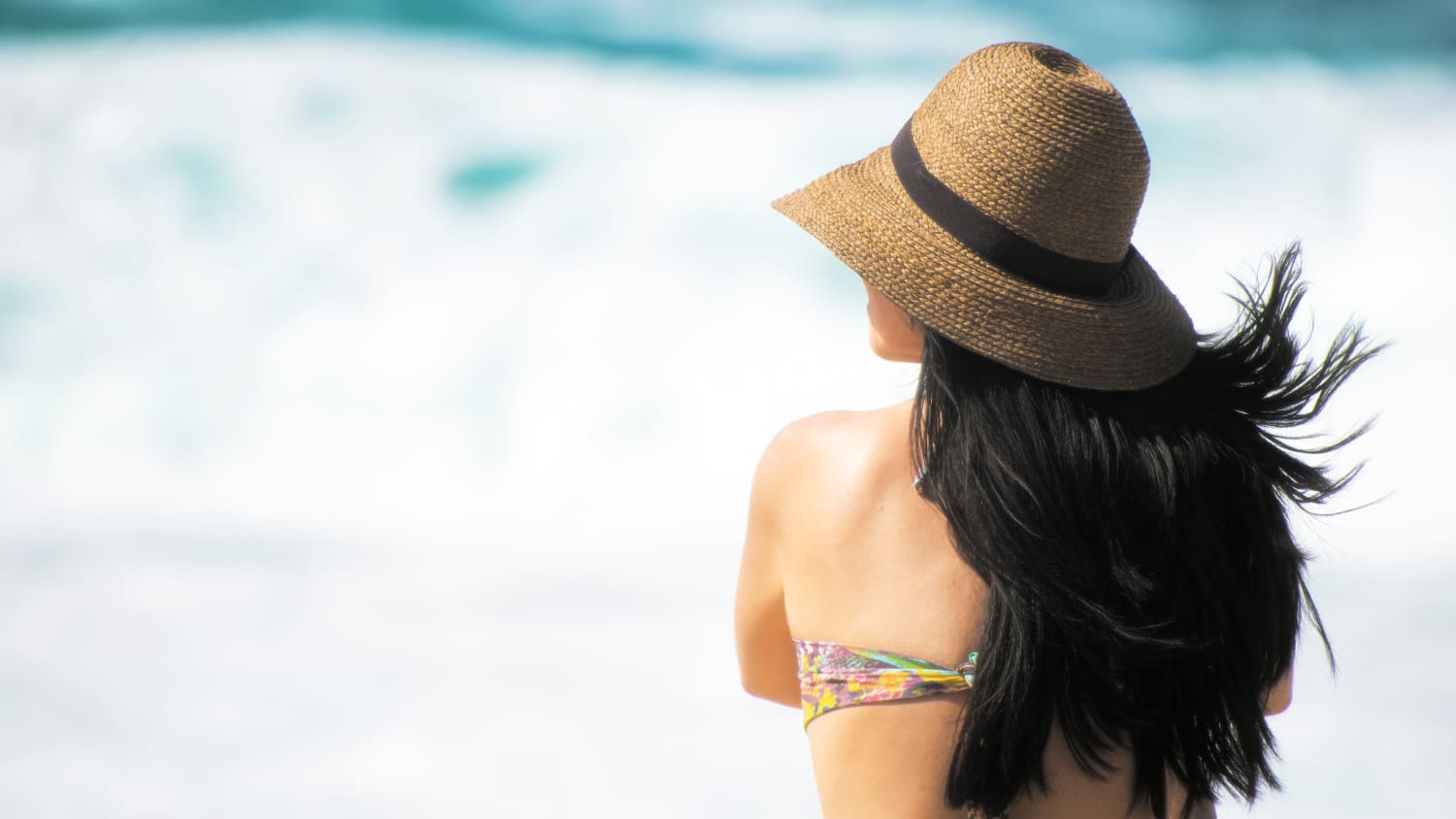 Woman on beach with long dark hair wearing hat.