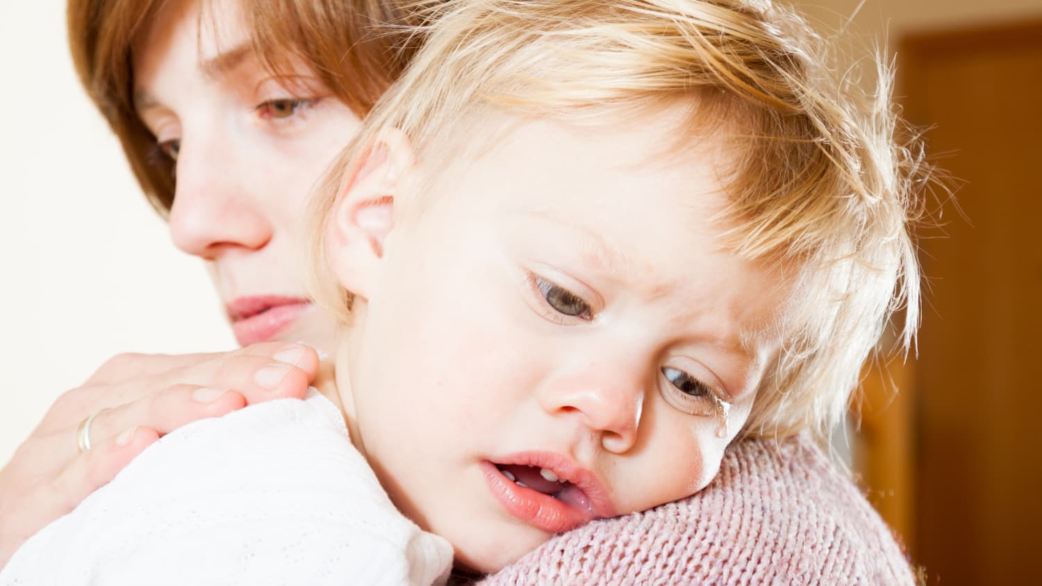 A mother holds her blonde toddler in her arms, comforting him.