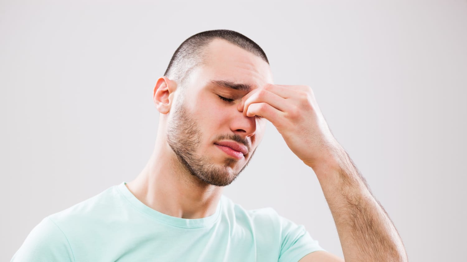 a young man who could be treated with sinus surgery tries to minimize the pain by pinching his nose