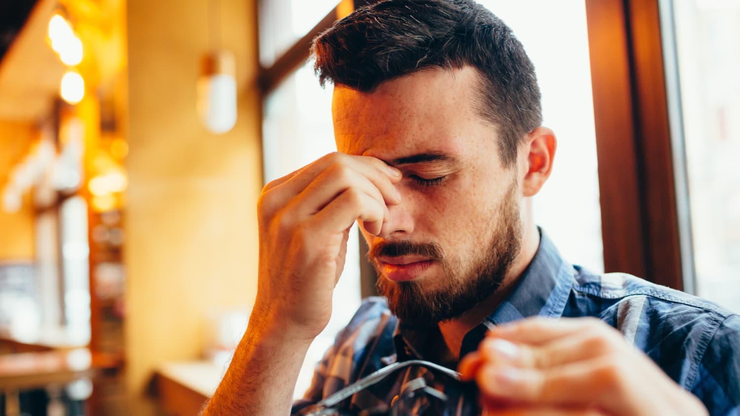 young man takes his glasses off and rubs his eyes possibly because of double vision