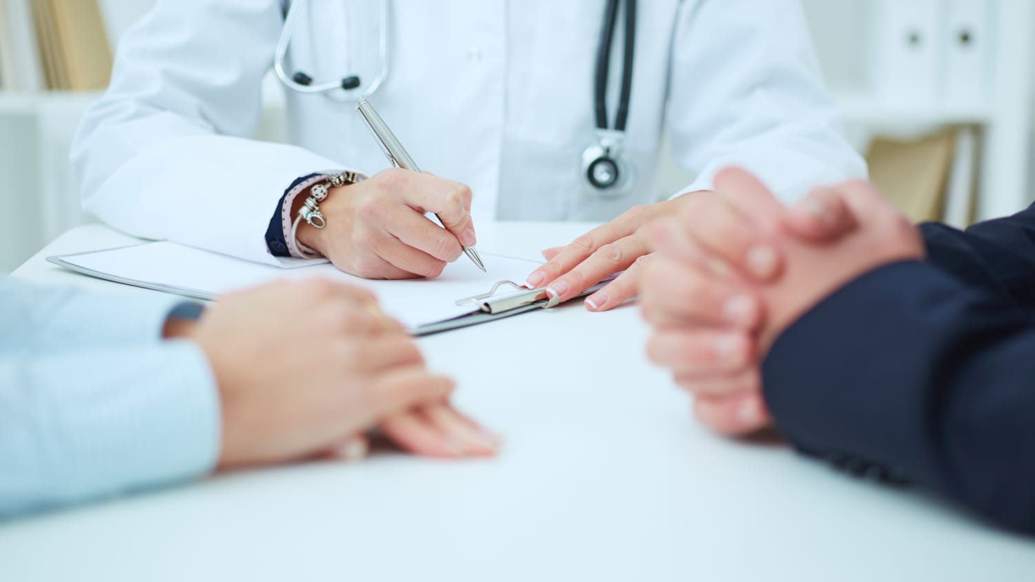 Doctor wearing a stethoscope takes notes during a discussion about a patient's kidney transplant.