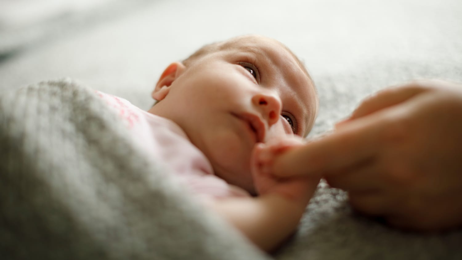 A newborn grabbing an adult's finger, possibly the result of egg freezing