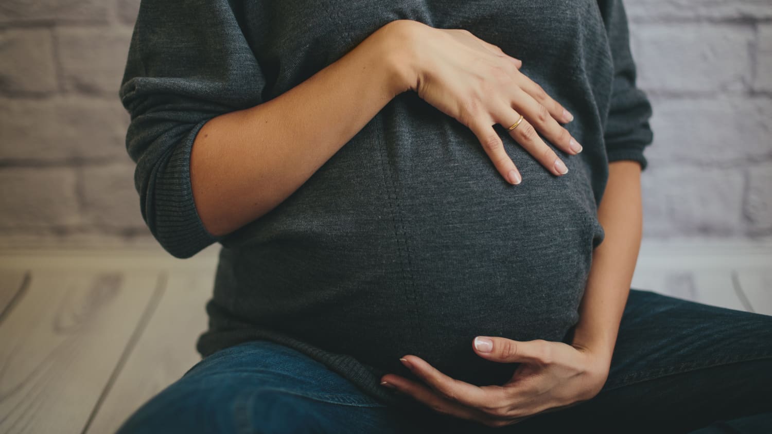 A close up of a woman's pregnant belly under a long sleeved gray shirt. She possibly has a high-risk pregnancy.