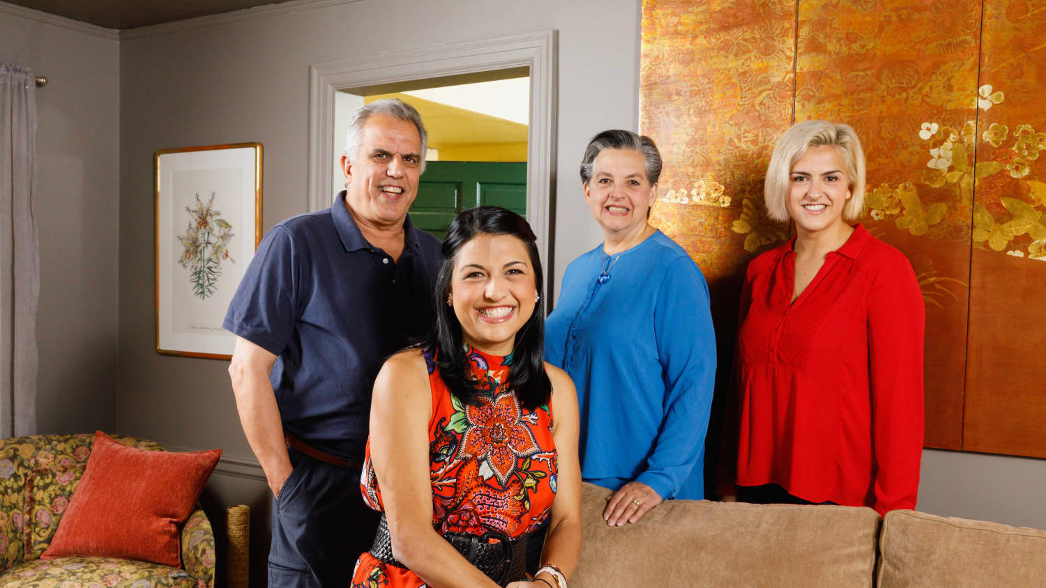 Amanda in a red patterned dress sits on a tan couch in her family's living room with her Mom, Dad and Sister standing behind her.