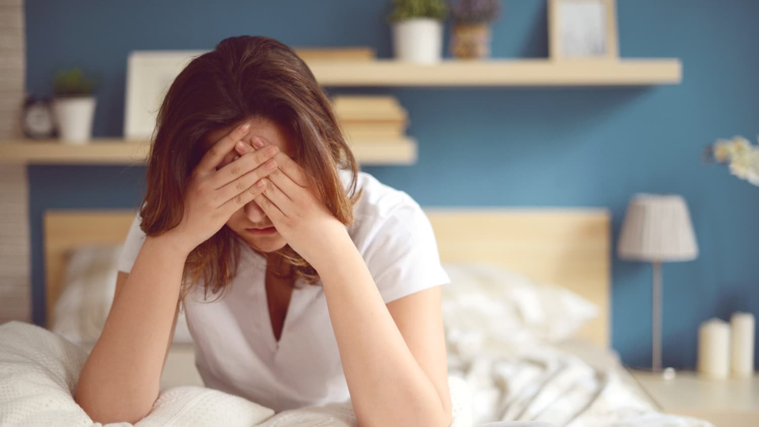 A woman sit ups in bed with her face in her hands, possibly because she has endometriosis