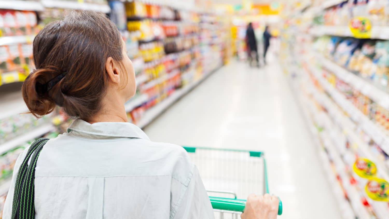 A woman in a button down shirt is pushing a shopping cart. She feels like she may have a nosebleed. 