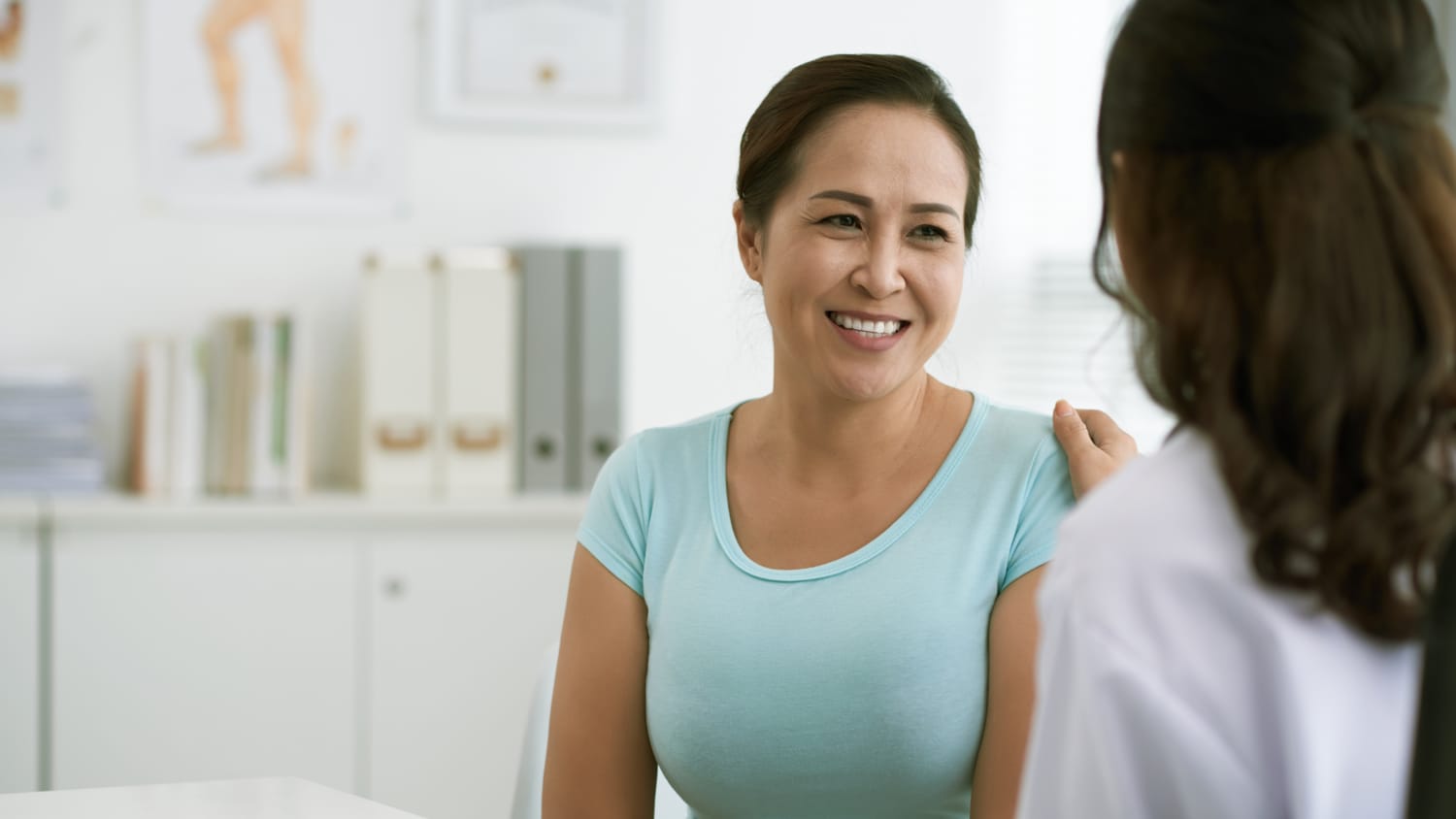 A woman in a blue short sleeved shirt talks to her doctor about rectal bleeding