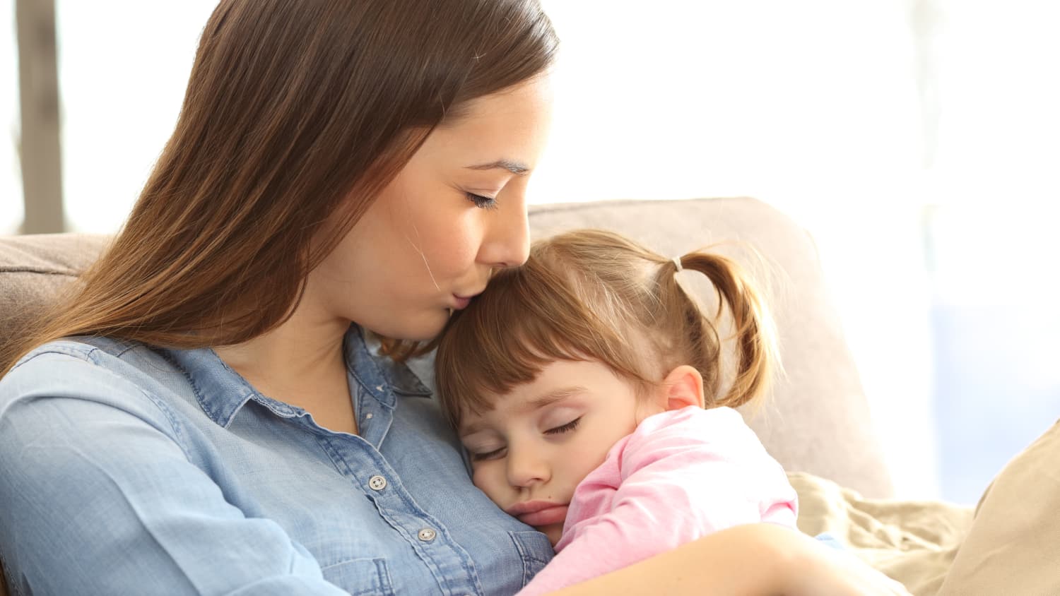 Close up portrait of a mother kissing her young daughter, who possibly has pediatric asthma.