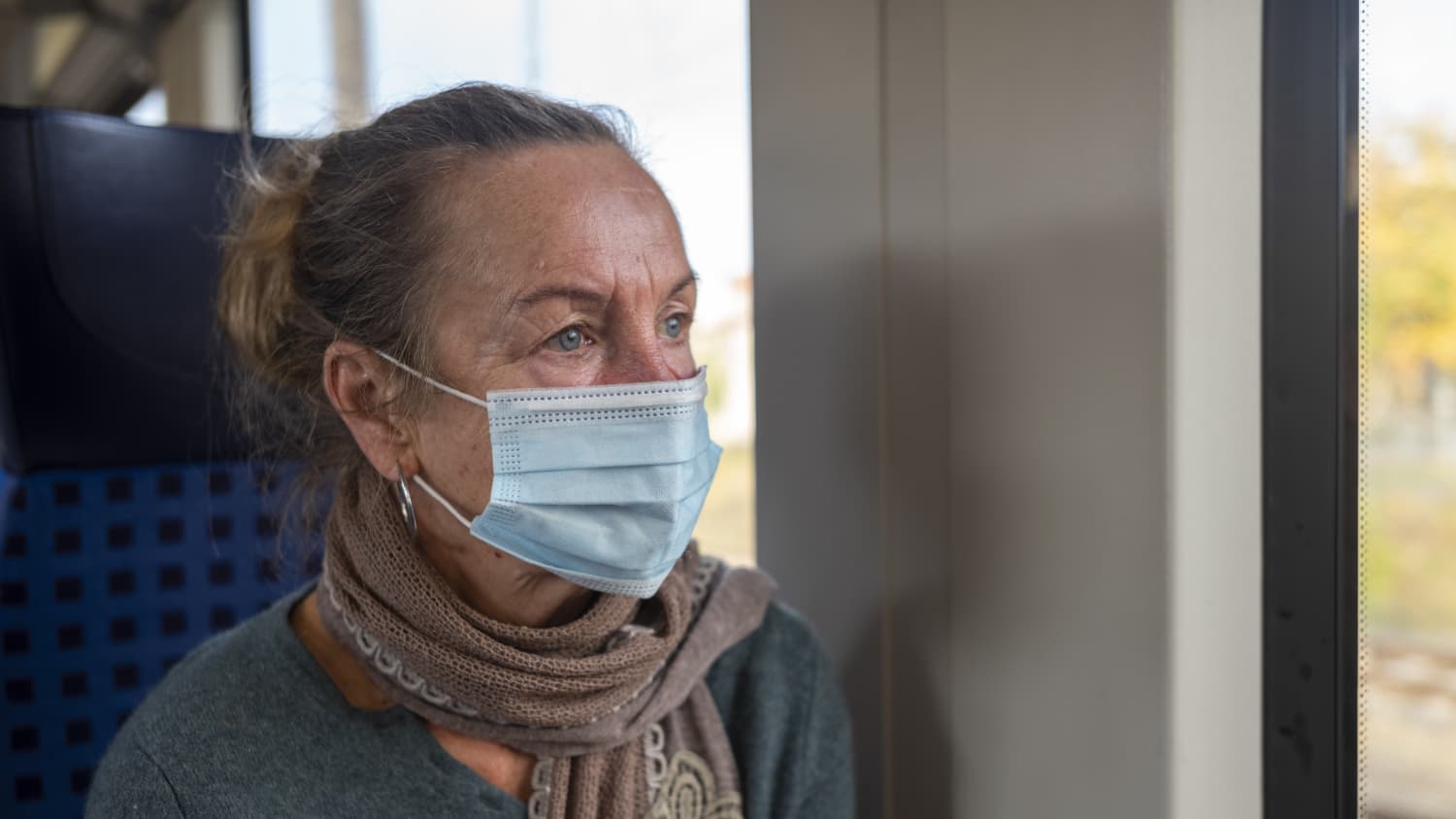 older woman practicing strategic masking on a train to protect against COVID