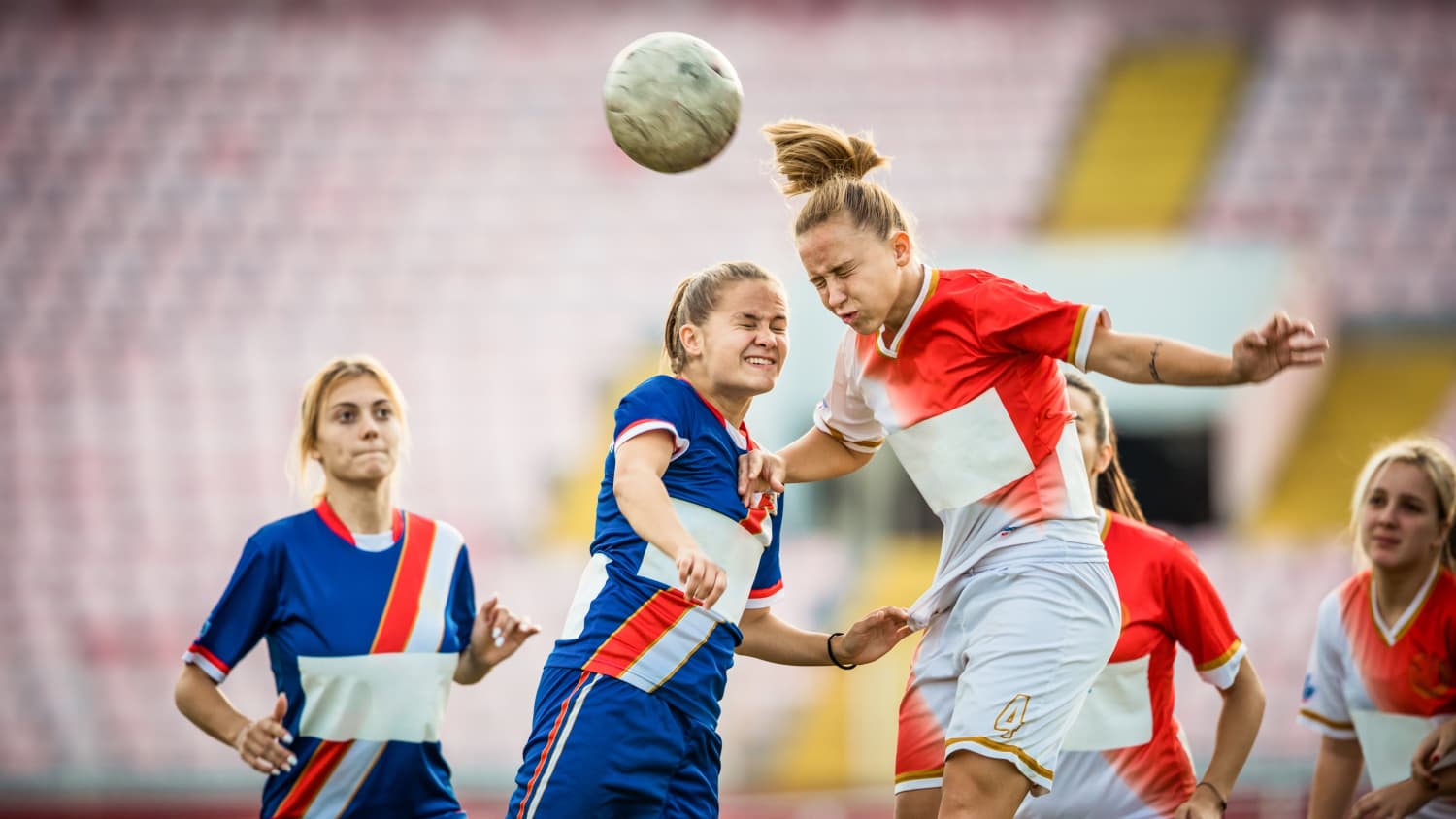 Two female soccer rivals heading the ball on a match, possibly at risk for concussion