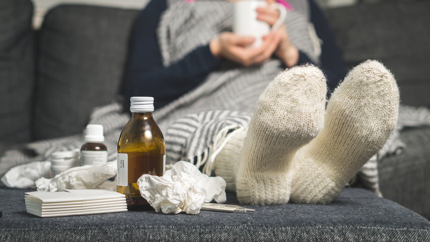 A person with the flu wearing pajamas sips a cup of tea.