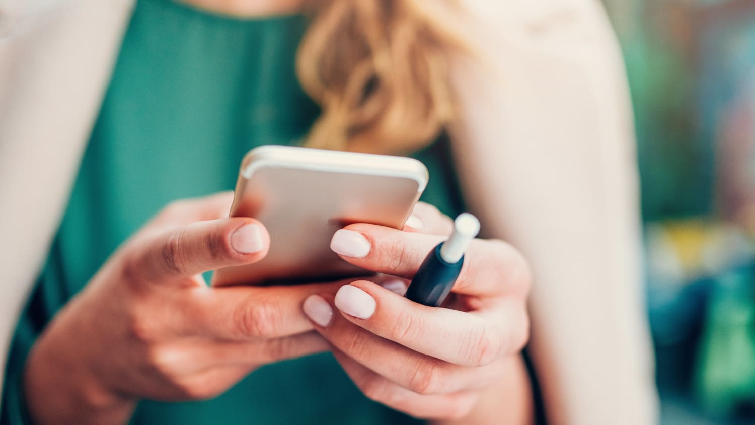 Young woman holding smart phone and an E-Cigarette for vaping in hands