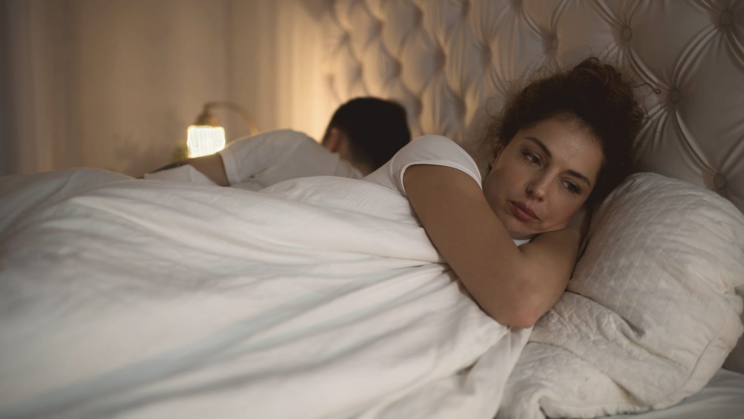 Woman lying in bed awake with her partner next to her asleep.