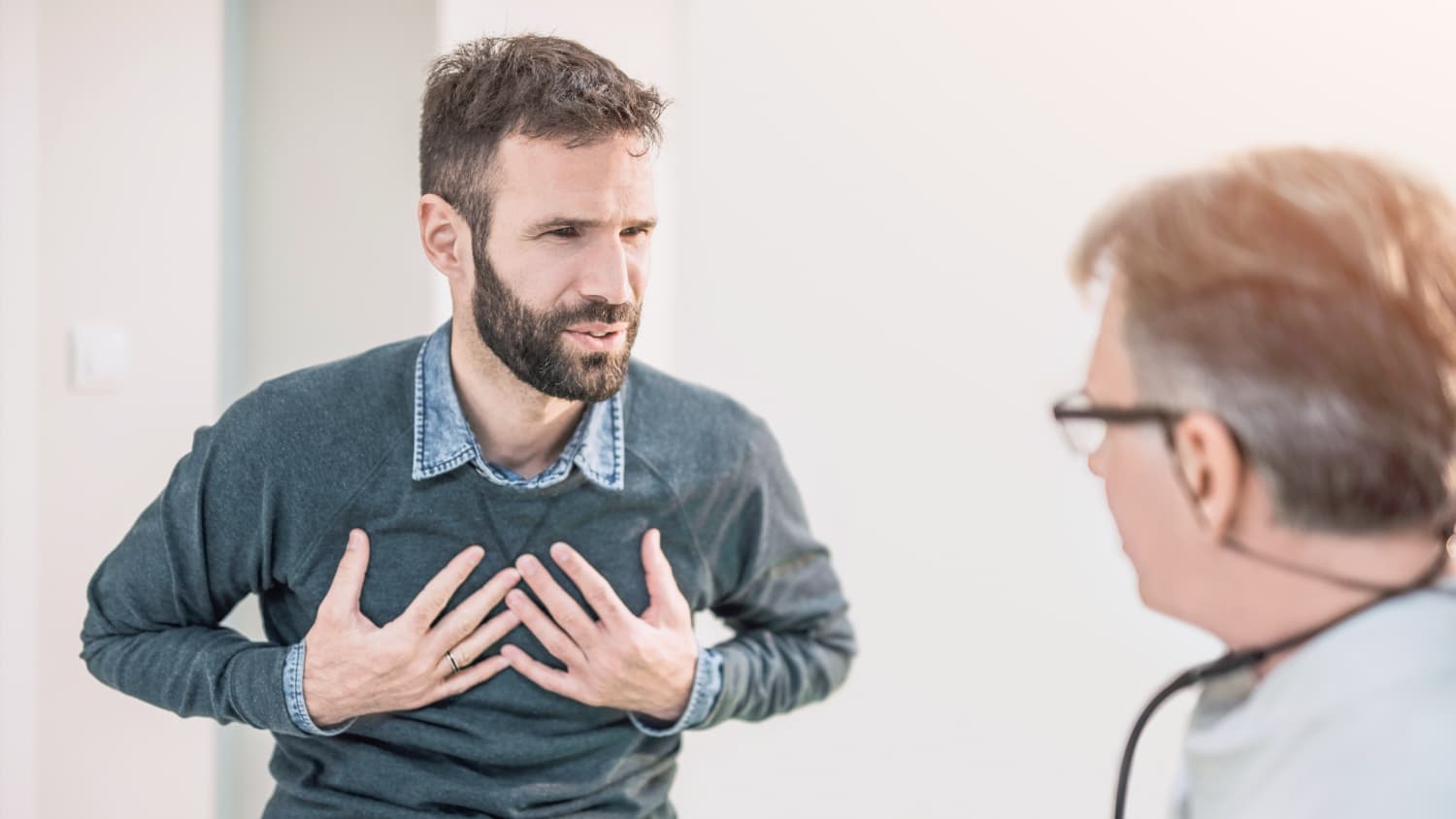 Man describes holds his chest while talking to his doctor about a possible adult congenital heart problem.