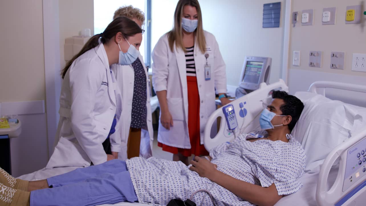 A patient in a hospital bed while a team of providers attend to him.