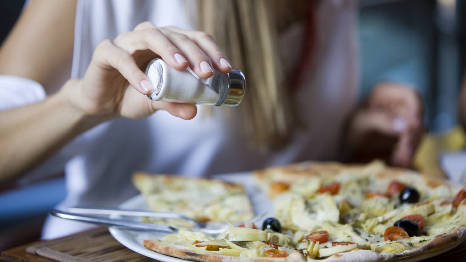 woman adding salt to pizza