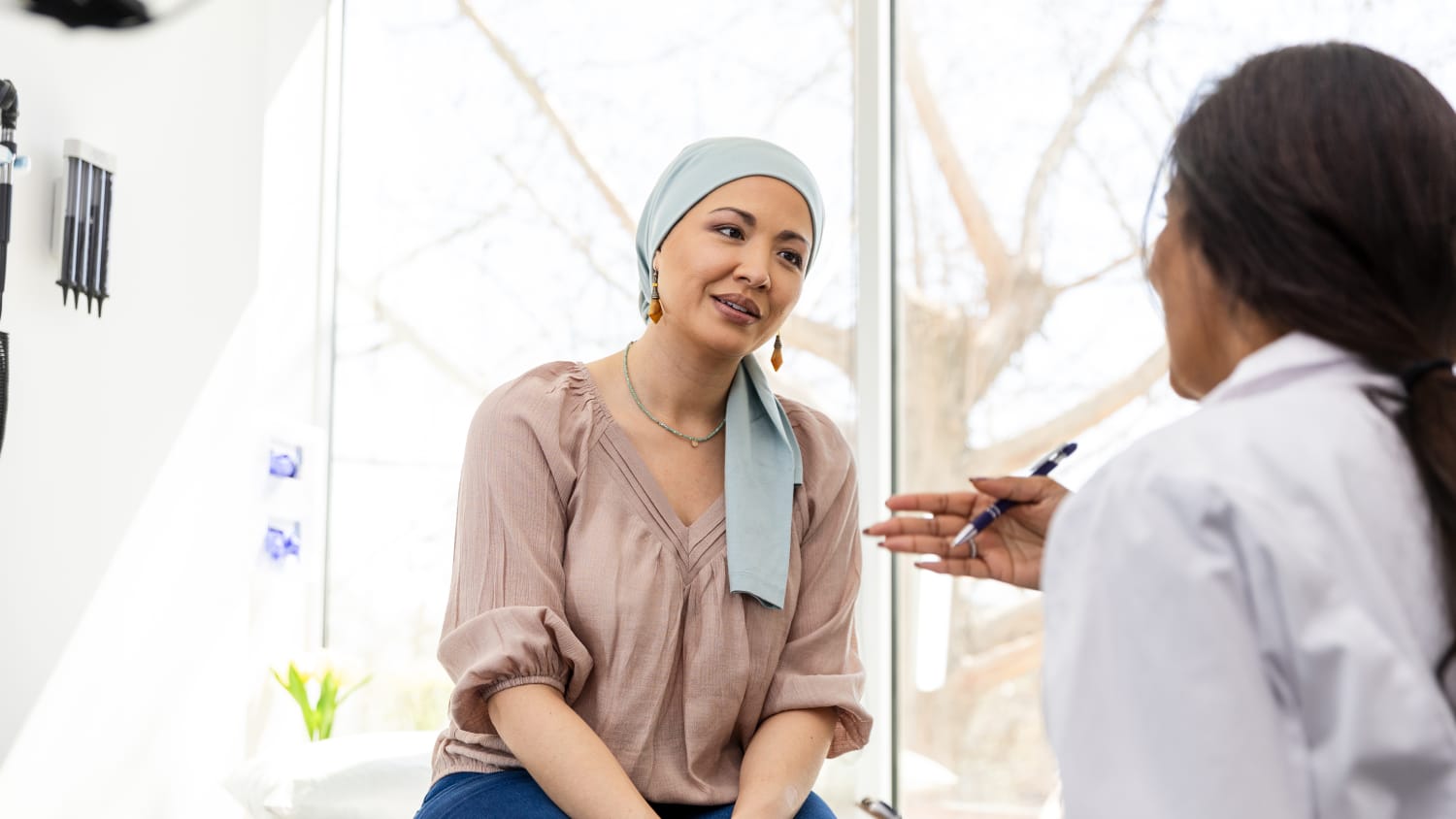 A woman wearing a headscarf talks to her cancer doctor in an exam room. 