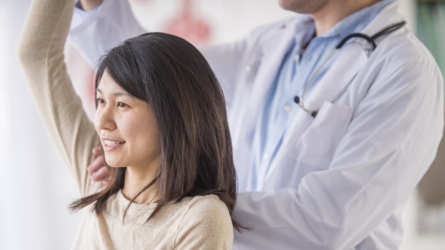 A woman who possibly has a rotator cuff injury raises her arm for a doctor