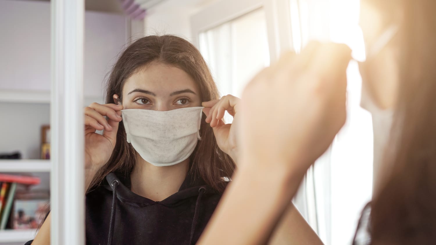 woman putting on a mask, possibly hiding maskne, in front of a mirror