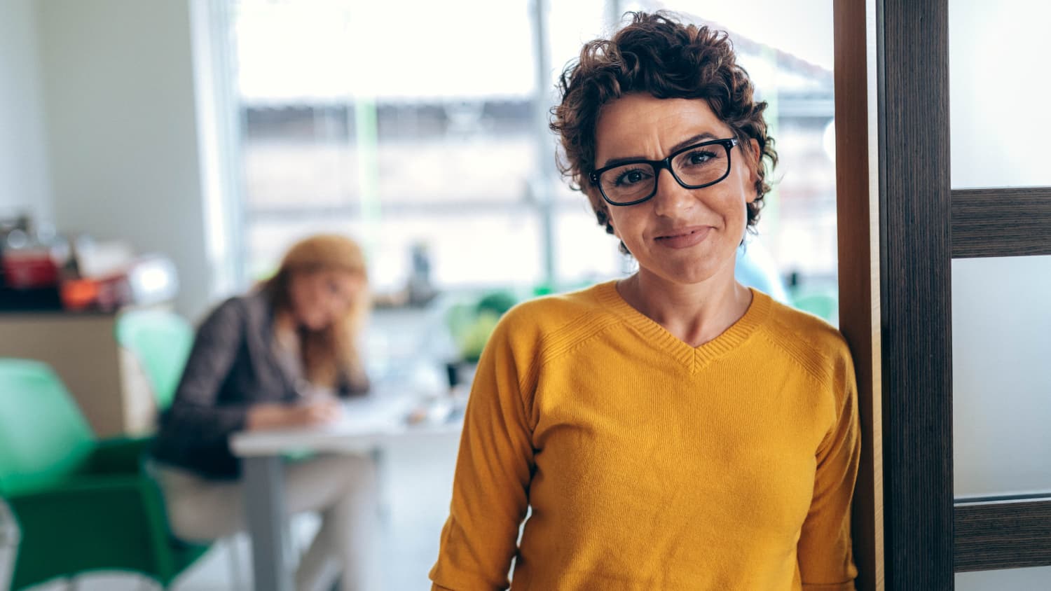 mature woman standing in doorway smiling, possibly at receiving less chemotherapy for breast cancer treatment