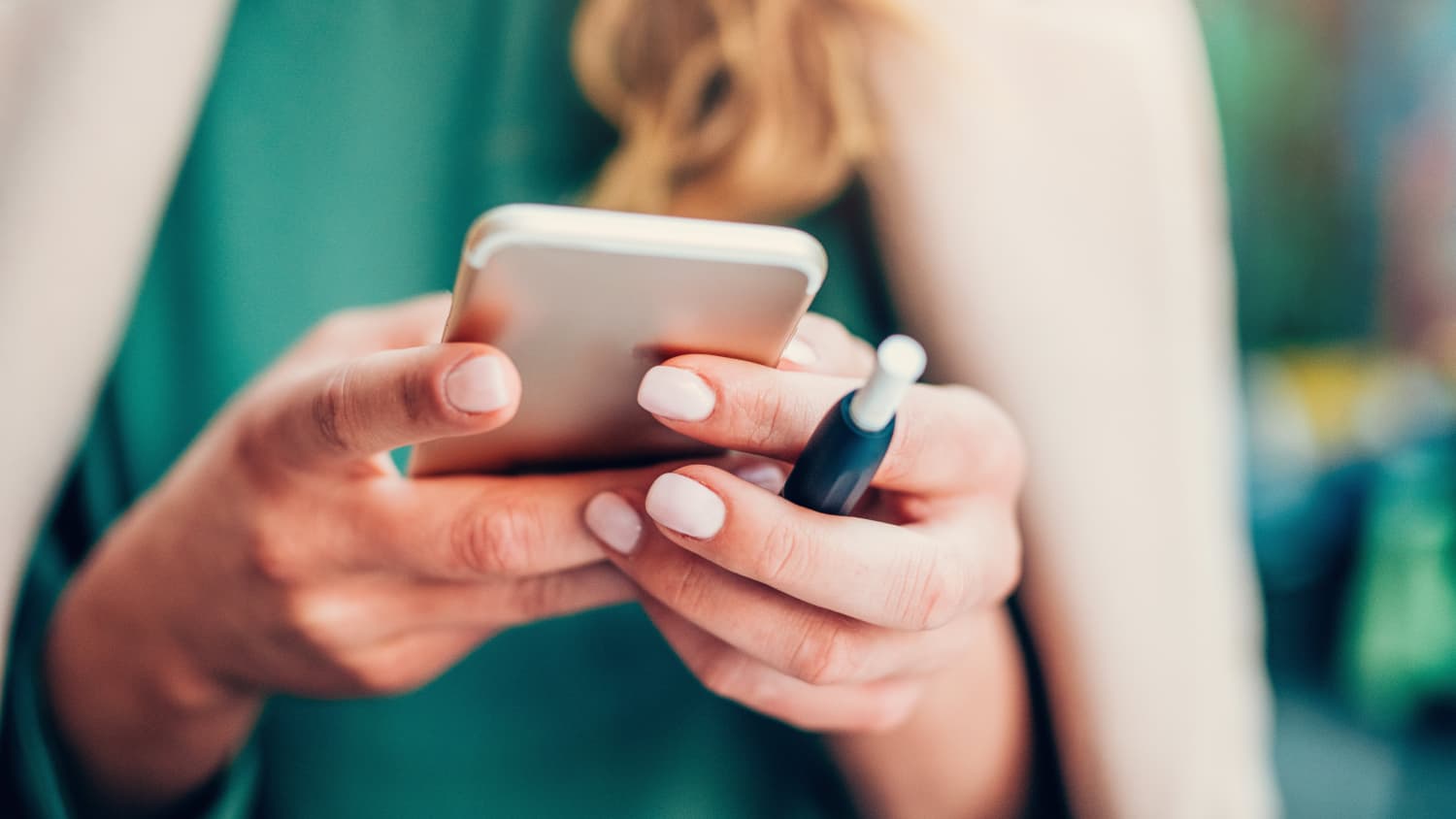 Young woman holding smart phone and an E-Cigarette for vaping in hands