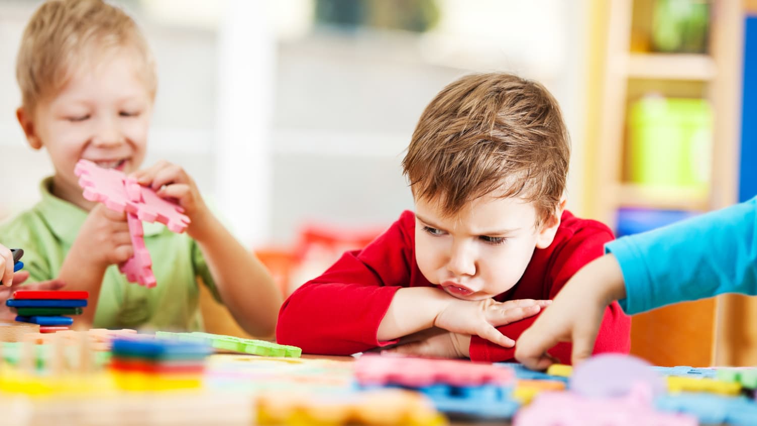 One small boy sulks while another plays in a setting where autism is treated with pivotal response syndrome.