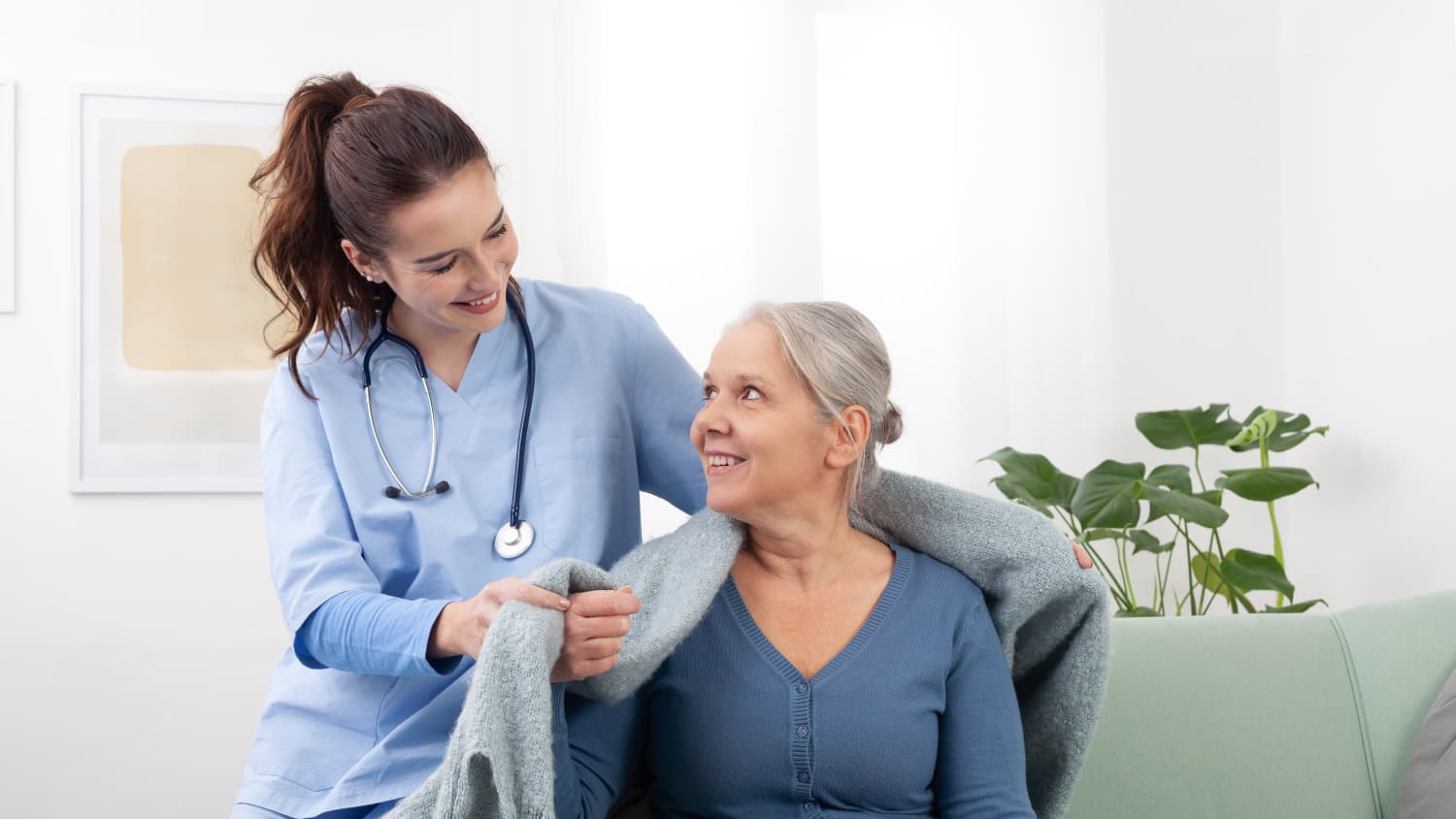 A nurse puts a blanket over the shoulder of a female palliative care patient.
