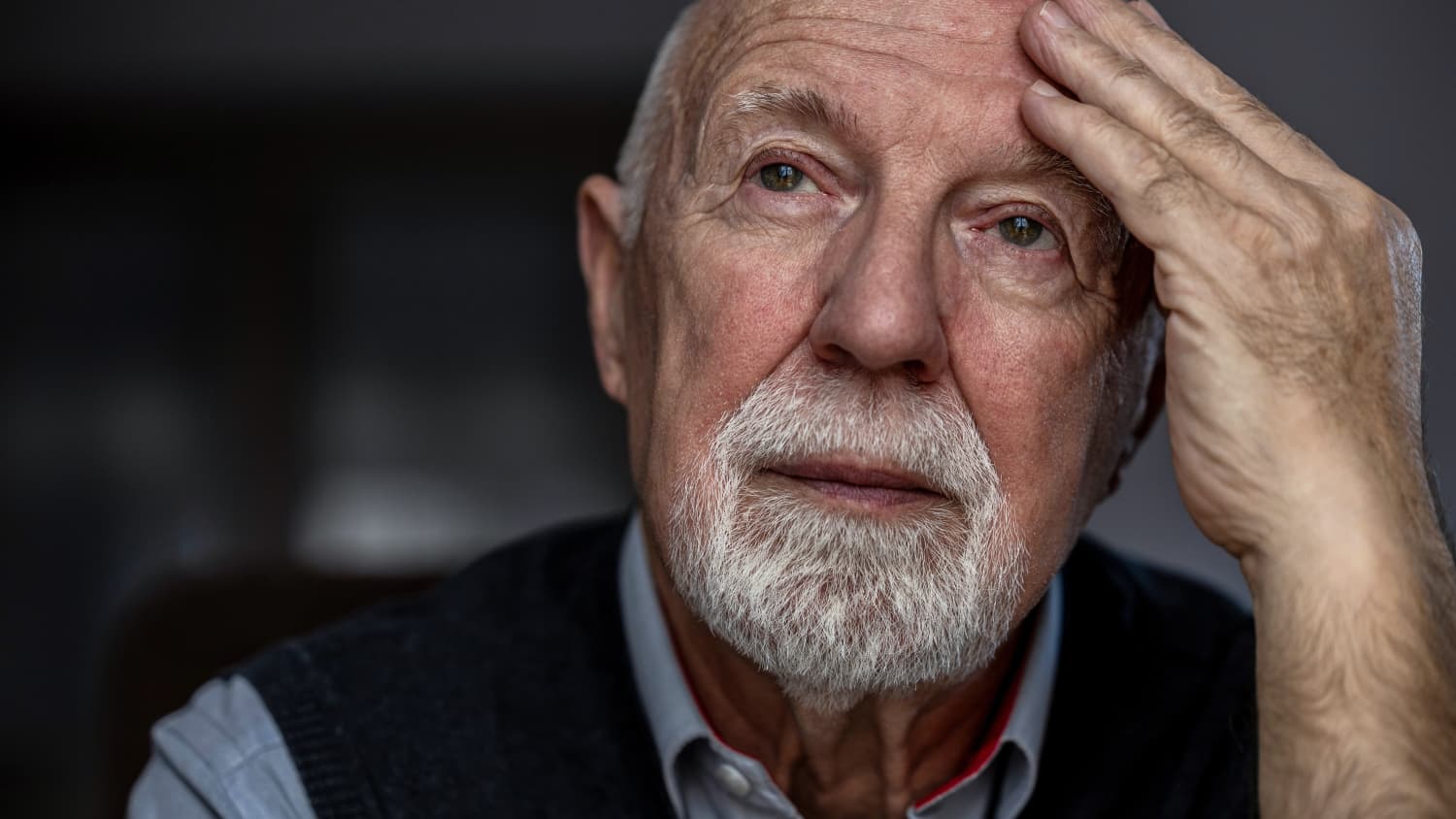 An older man with Alzheimer's disease places his hand on his forehead. 