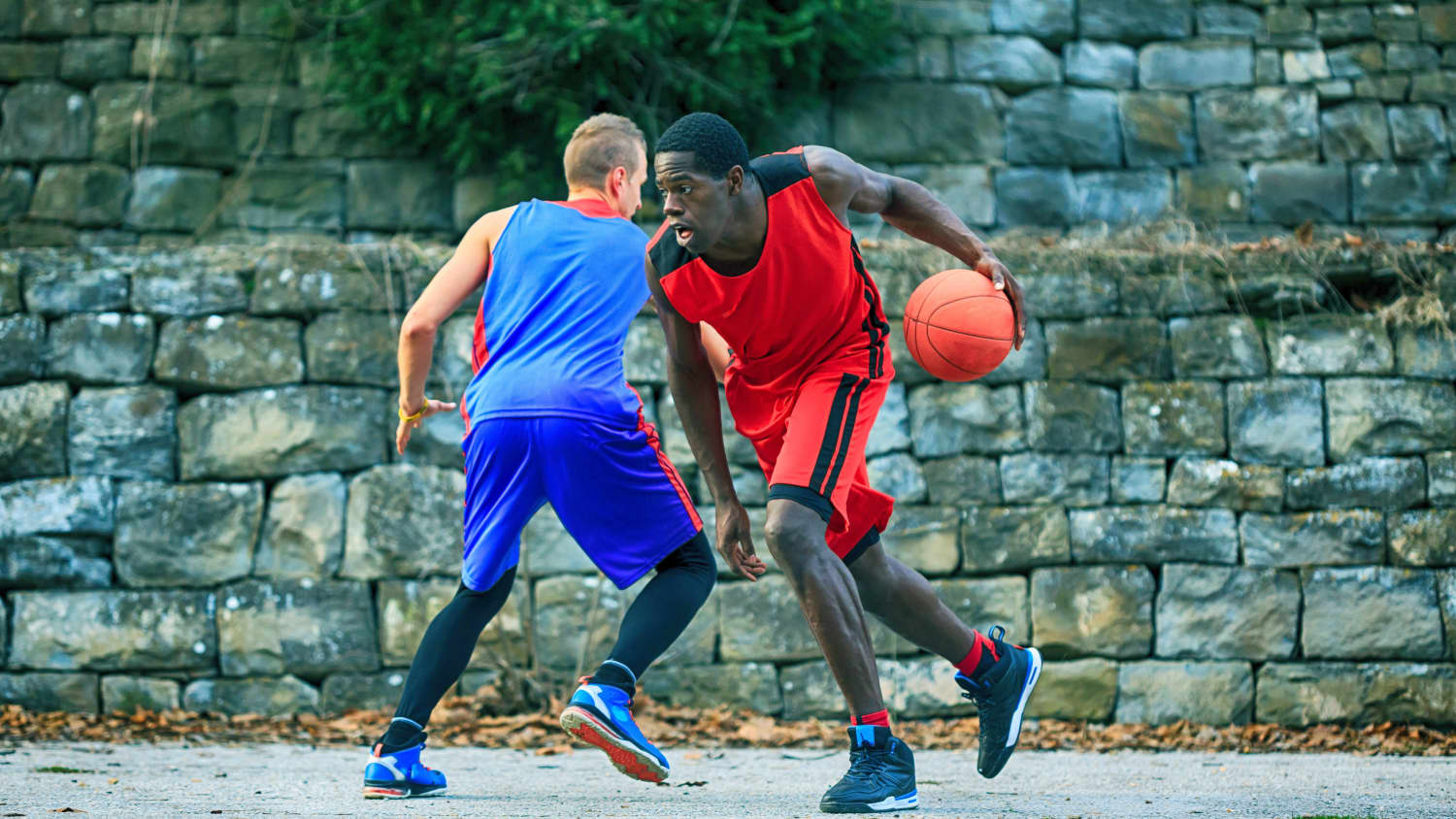 Two young people play basketball in a park.
