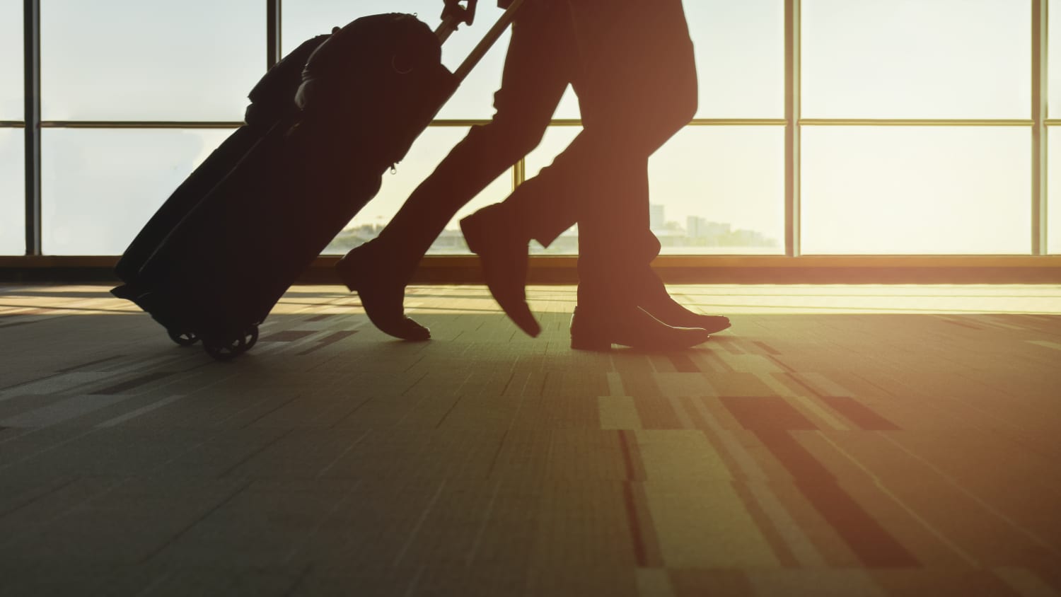 Travelers with luggage walking in the airport who are at risk of global health and travel-related maladies.