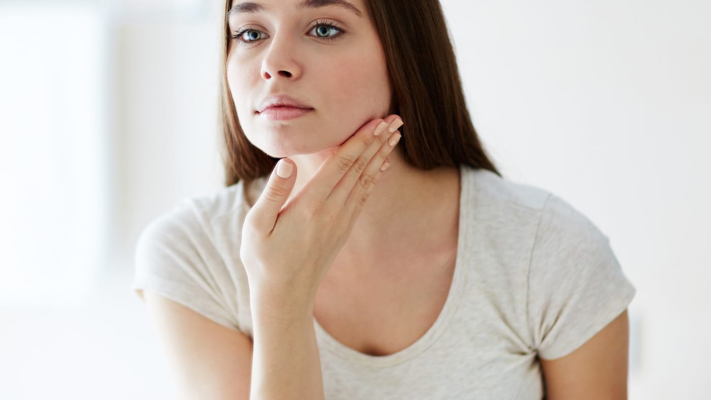 woman looking into a mirror, possibly considering at-home beauty products