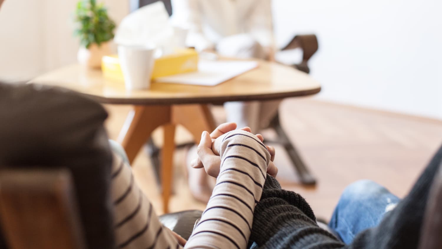 A couple sits, holding hands while listening to their doctor, possibly discussing a diagnosis of esophageal atresia for their child