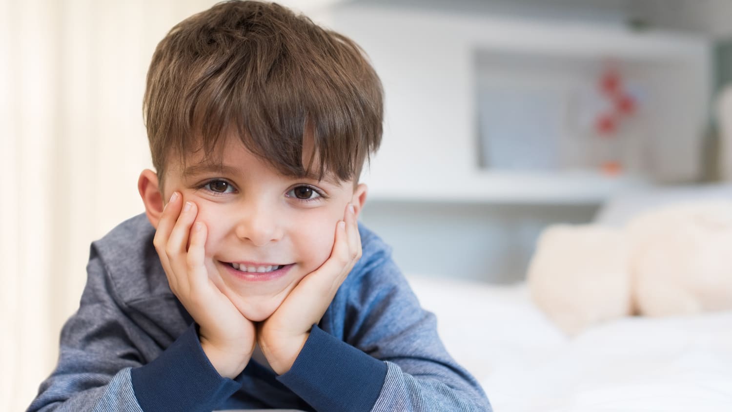 A young boy holds his head in his hands and smiles after treatment for pediatric incontinence