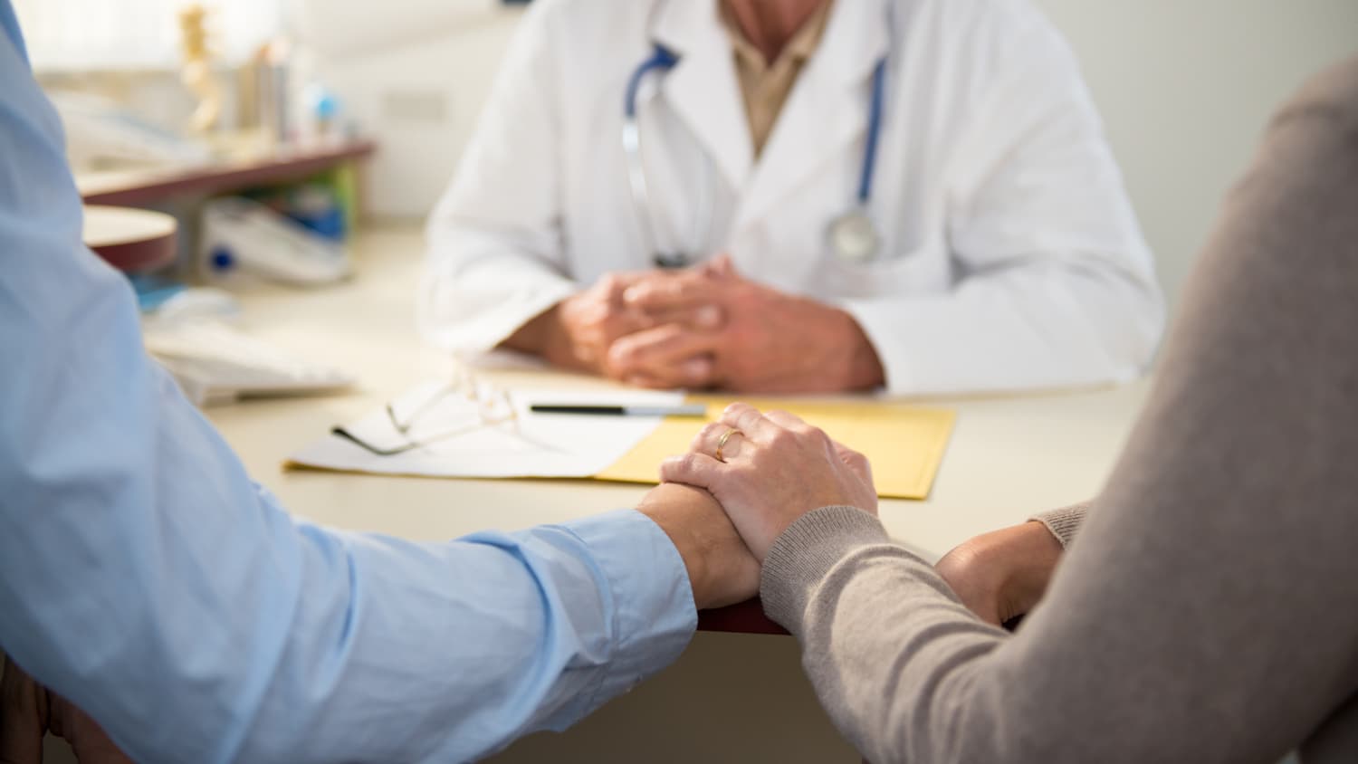 A couple holding hands talks to a doctor about imaging results.