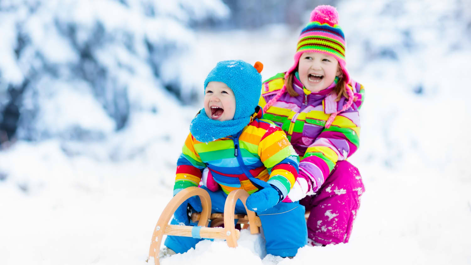 Two children are sledding while wearing colorful outerwear.