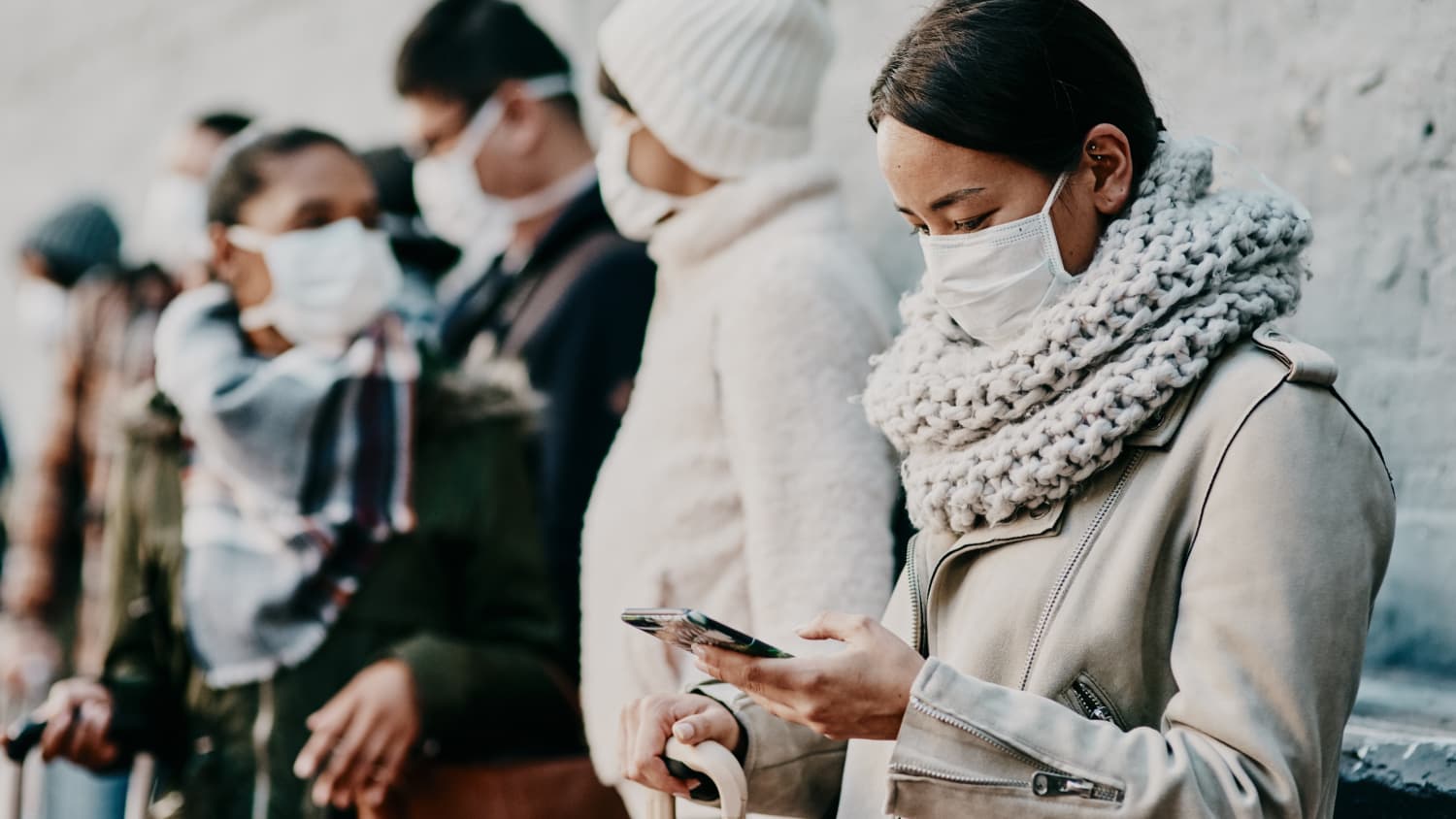 woman in a mask waiting on line while reading her phone, possibly learning of SalivaDirect, the new COVID-19 saliva tes