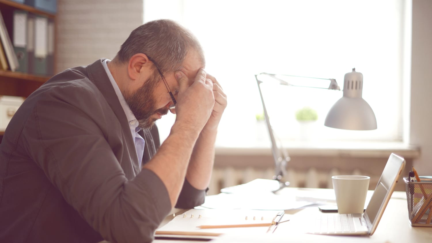 A man suffering from chronic stress holds his head in his hands at his desk.