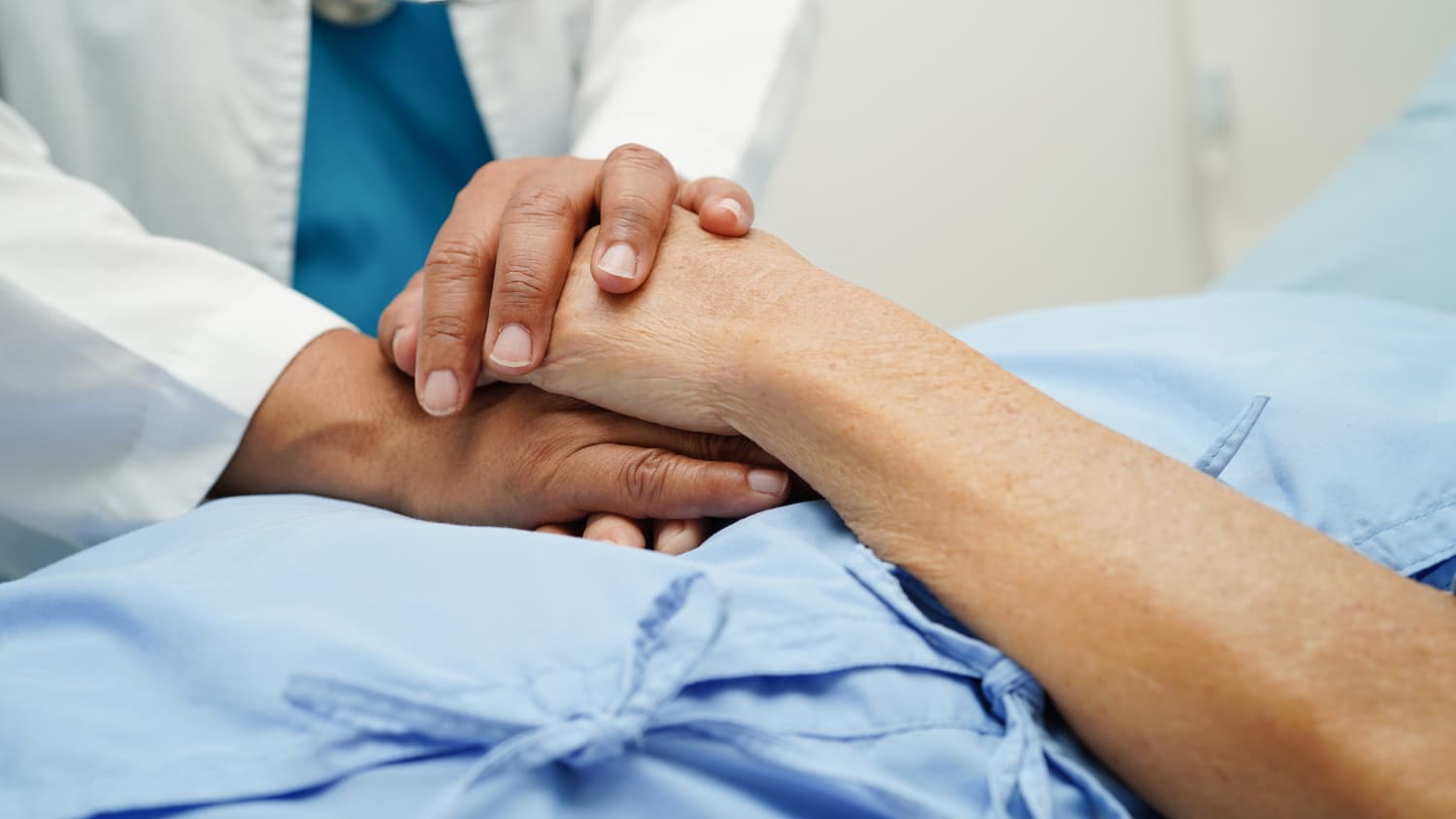 A doctor hold's a palliative care patient's hand in a hospital. 