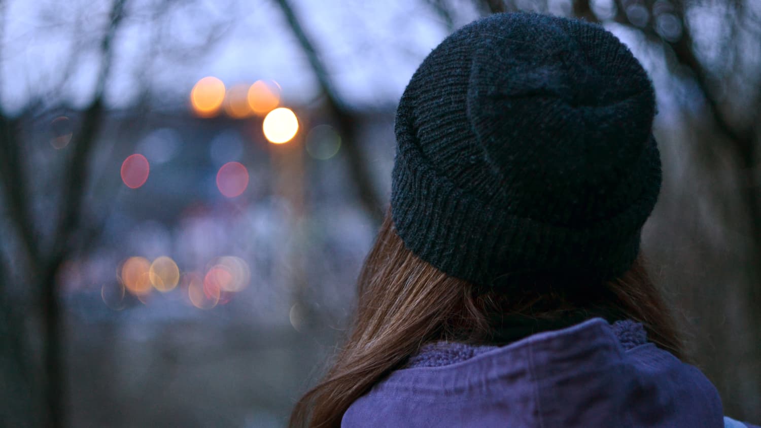 A woman, who possibly has bipolar disorder, stands with her back to the camera at night