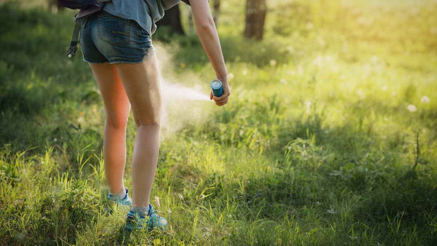 A girl standing in the woods applies insect repellent to protect against ticks, bites from which can cause alpha-gal syndrome. 