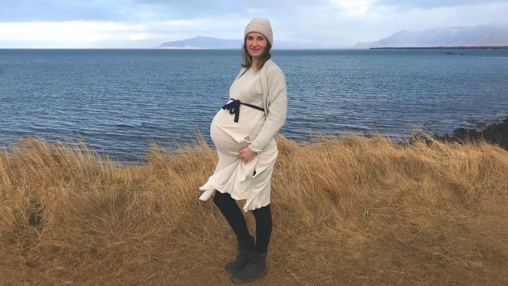 A pregnant woman stands in front of Icelandic scenery.