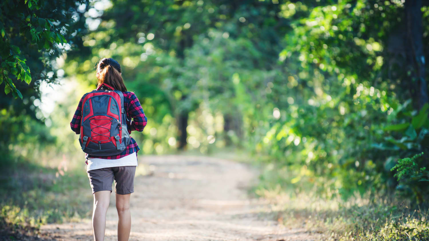 A woman with a backpack on hiking through the woods. She possibly recovered from sacroiliac joint fusion.