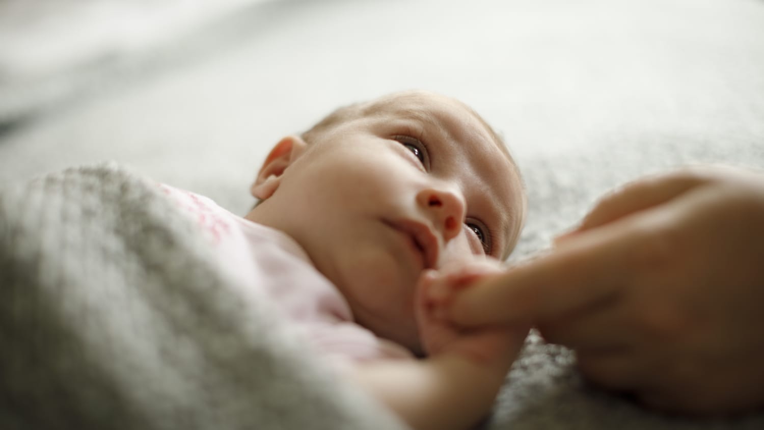 A newborn grabbing an adult's finger, possibly the result of egg freezing