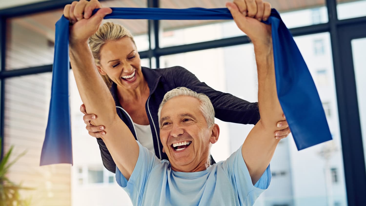 Photograph of a physical therapist helping a senior patient stretch with a stretch band in her office, possibly as part of cancer rehabilitation