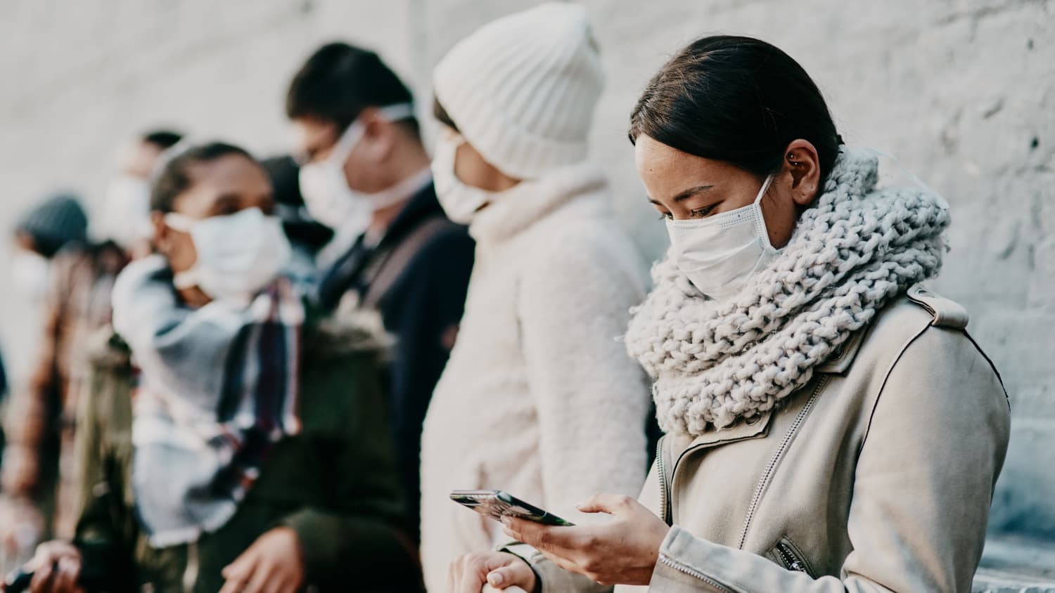 woman in a mask waiting on line while reading her phone, possibly learning of SalivaDirect, the new COVID-19 saliva tes