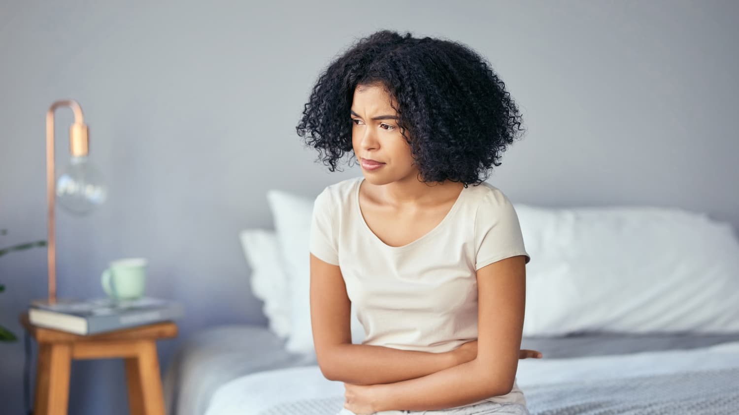 A woman with diverticulitis sits on a bed clutching her stomach.